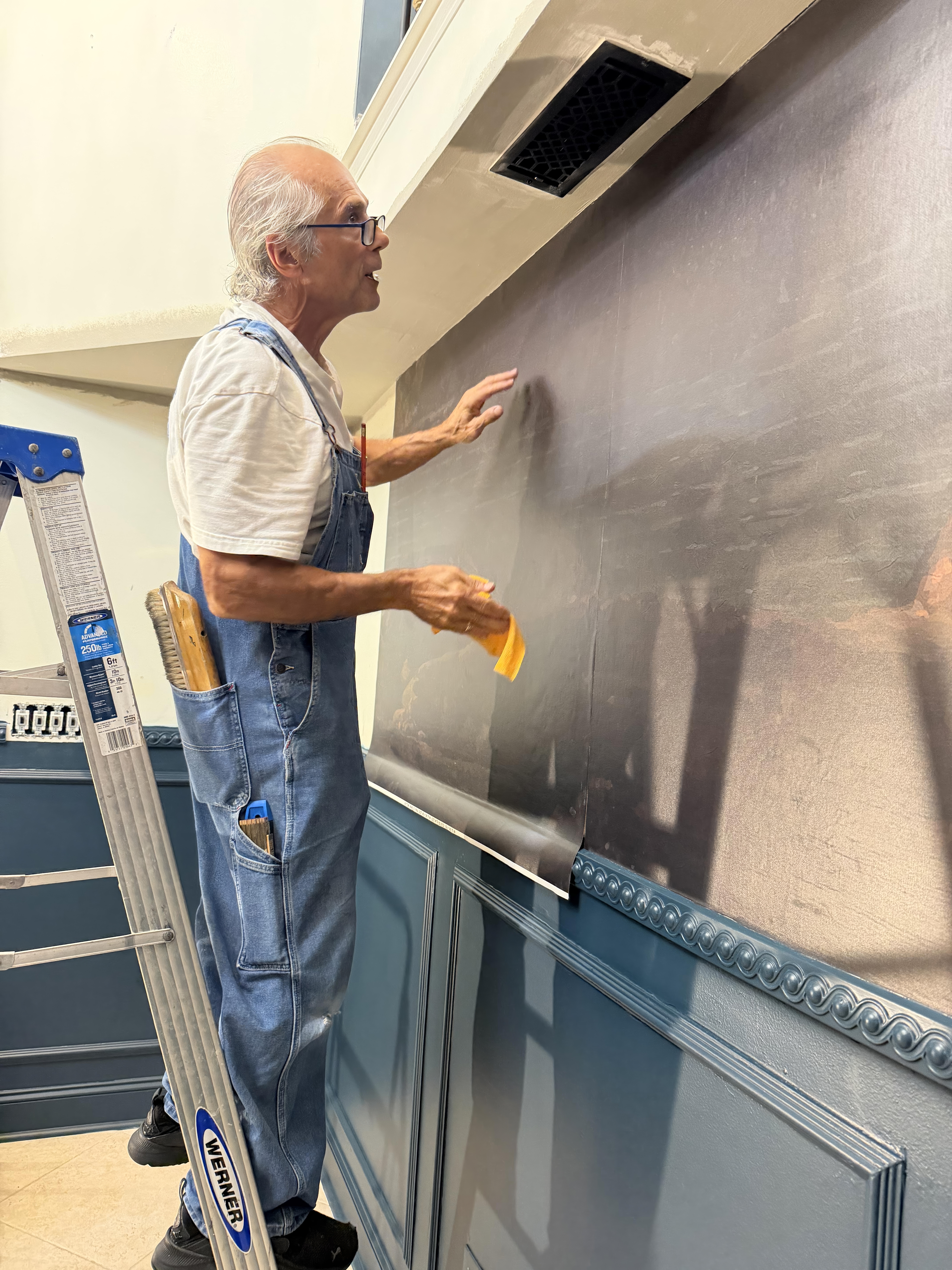 George Kazameas smoothing a mural panel near the ceiling line