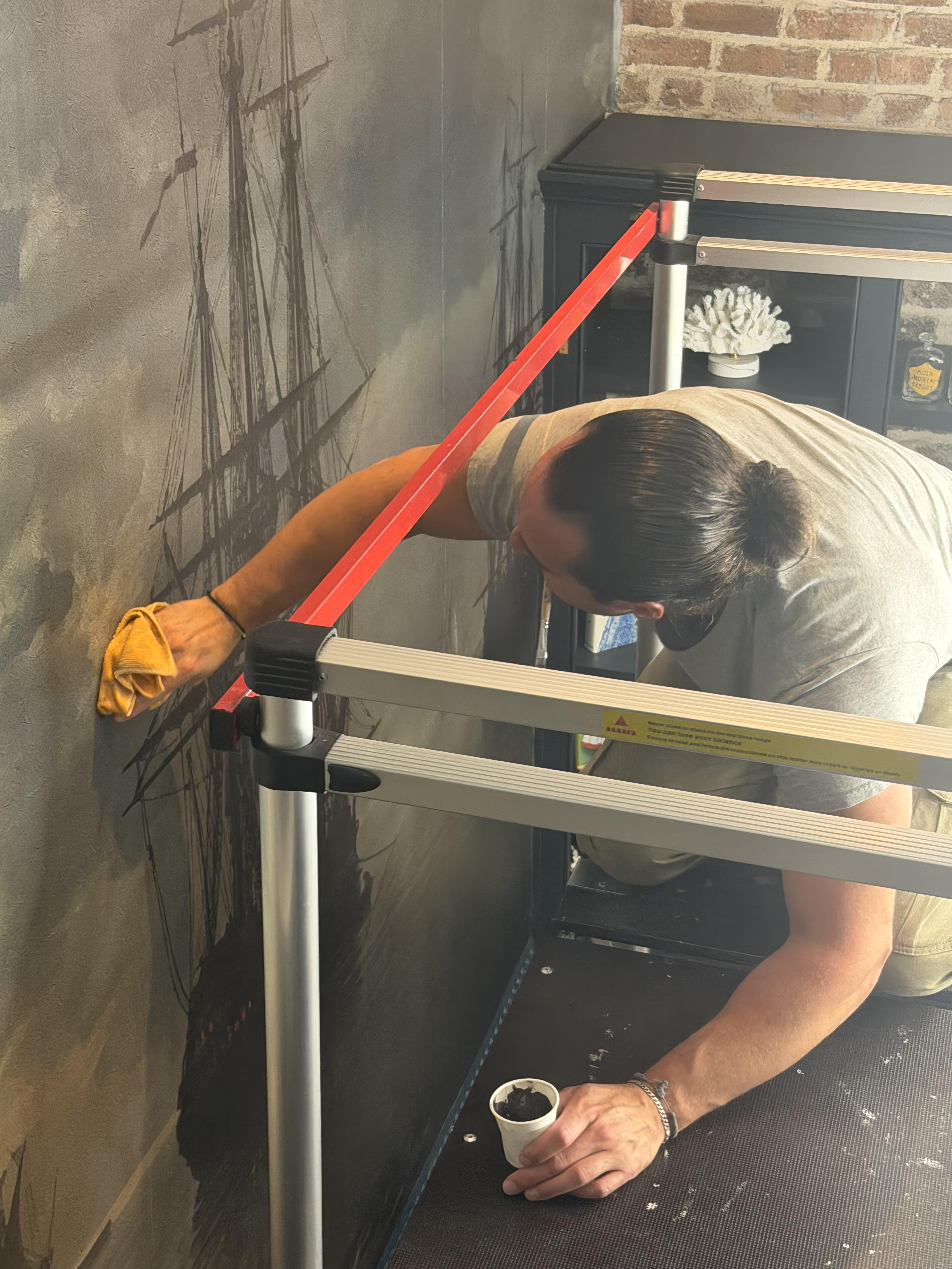 Constantine Kazameas finishing a mural seam near an exposed brick wall
